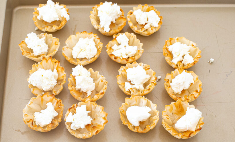 Phyllo cups filled with goat cheese on a baking sheet.