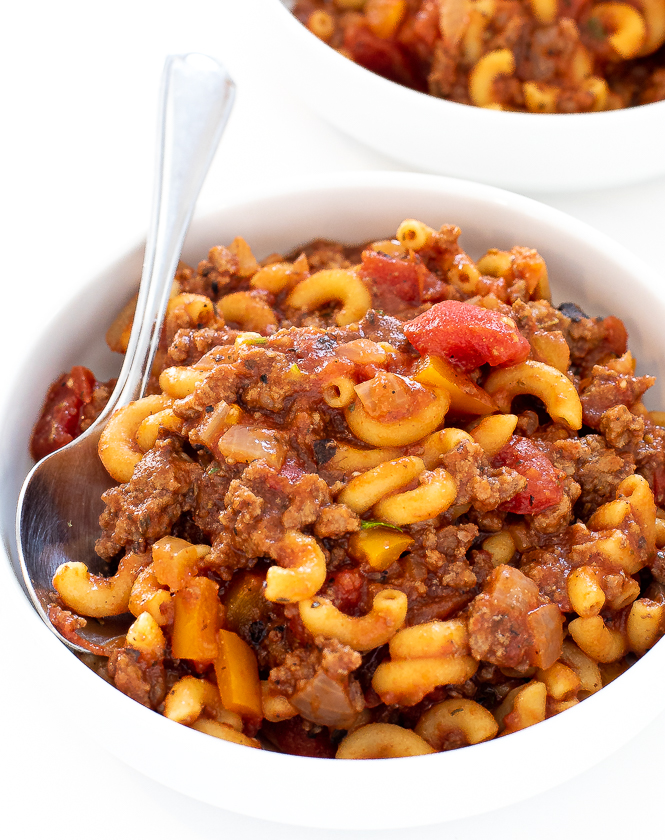 Crockpot goulash in a white bowl with a silver spoon.