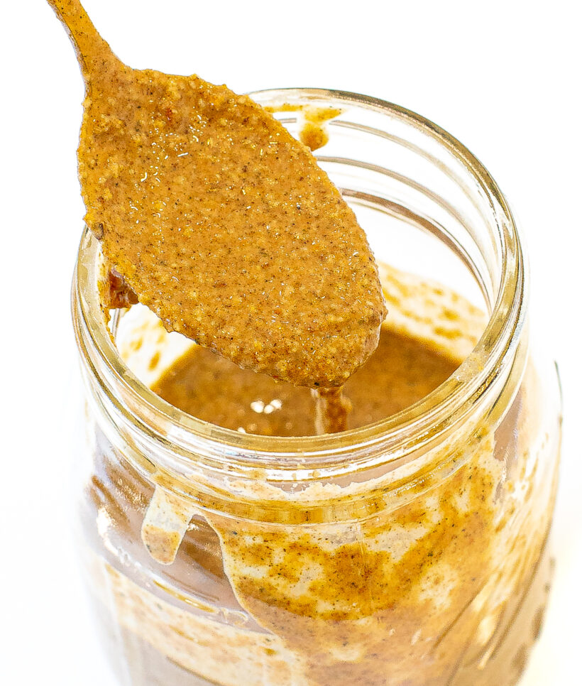 Spoon dipped in granola butter that is in a jar. 