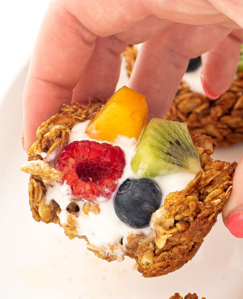 Hand holding a granola cup with a bite taken out of it.