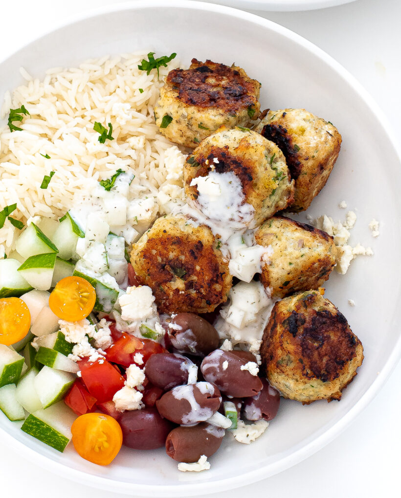Chicken meatballs with rice, veggies, feta and tzatziki sauce in a bowl.