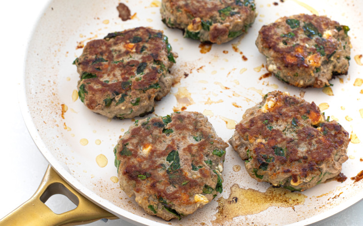 Turkey burgers being cooked in a white skillet. 