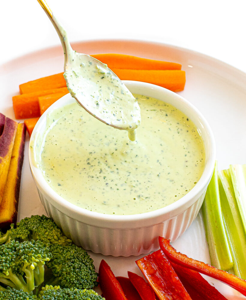 A spoon drizzling green goddess dressing into a bowl.