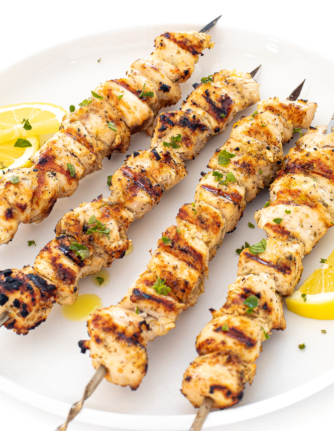 Grilled chicken skewers on a serving platter with lemon slices.