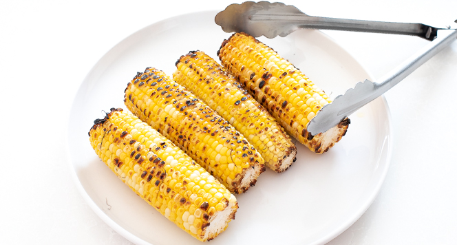 Grilled corn on a white plate with tongs