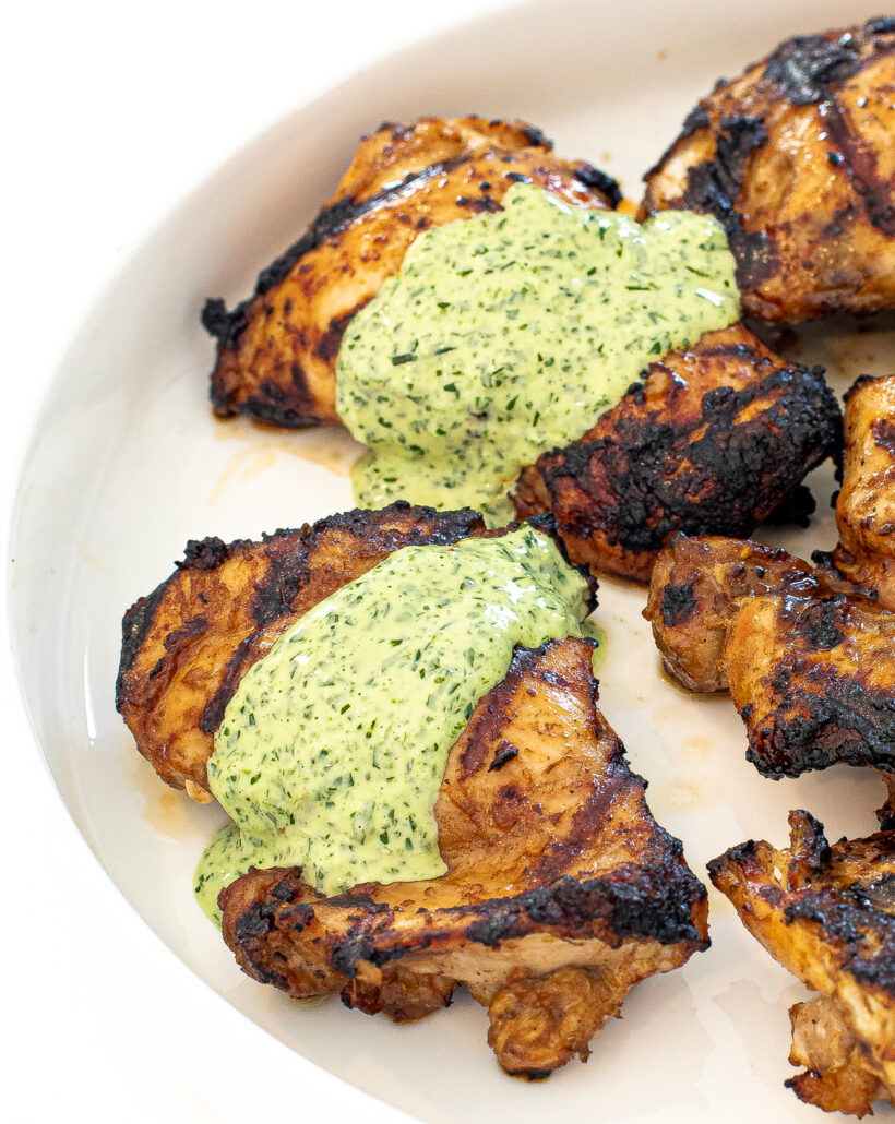 Chicken thighs on a white plate with green sauce on top. 