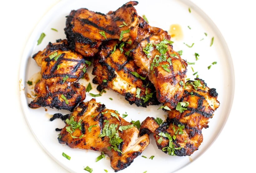 cooked thai grilled chicken on white plate with fresh herbs on top