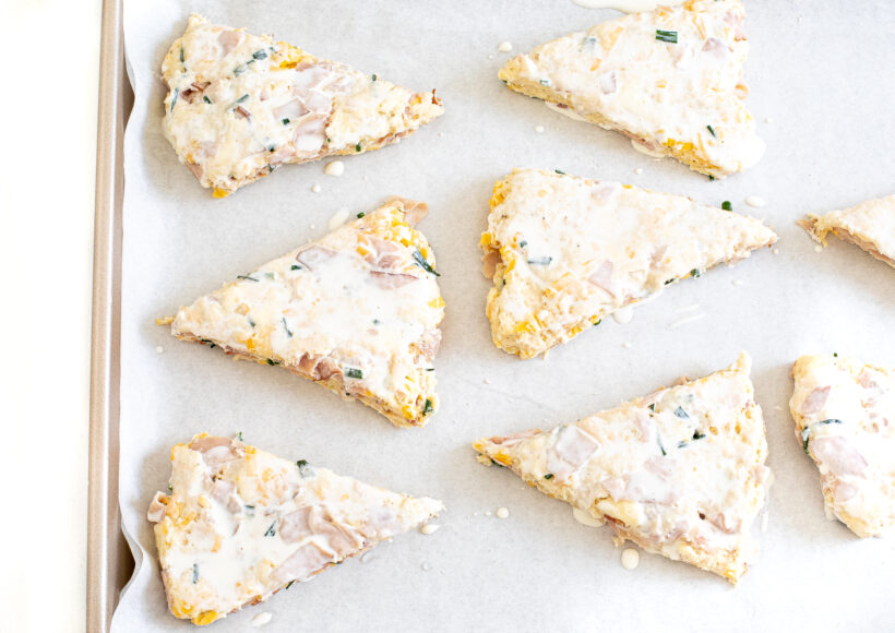 Ham and cheese scones in the shape of triangles on a baking sheet before being baked. 