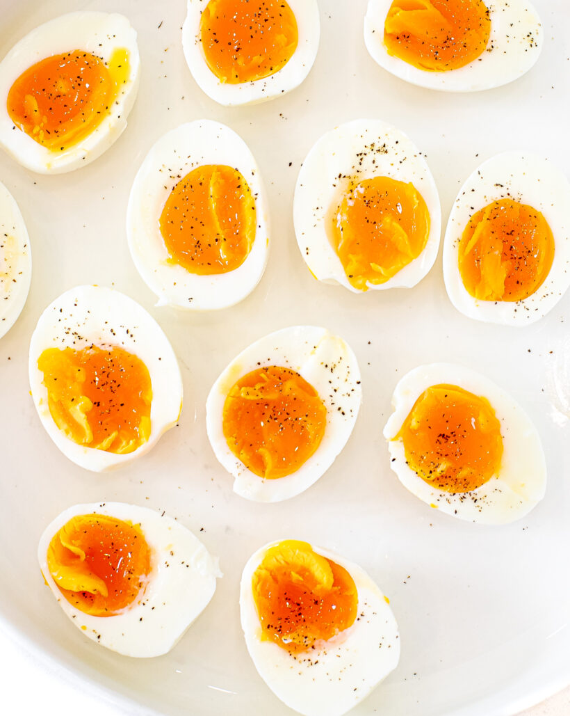 Overhead shot of jammy eggs served on a plate sprinkled with pepper.