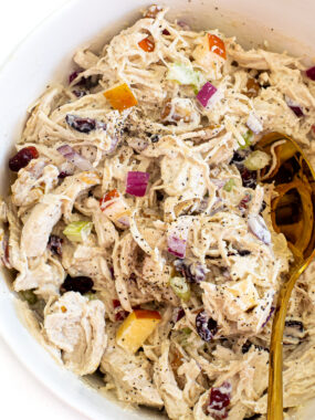 A white bowl with harvest chicken salad. A gold spoon is in the salad.