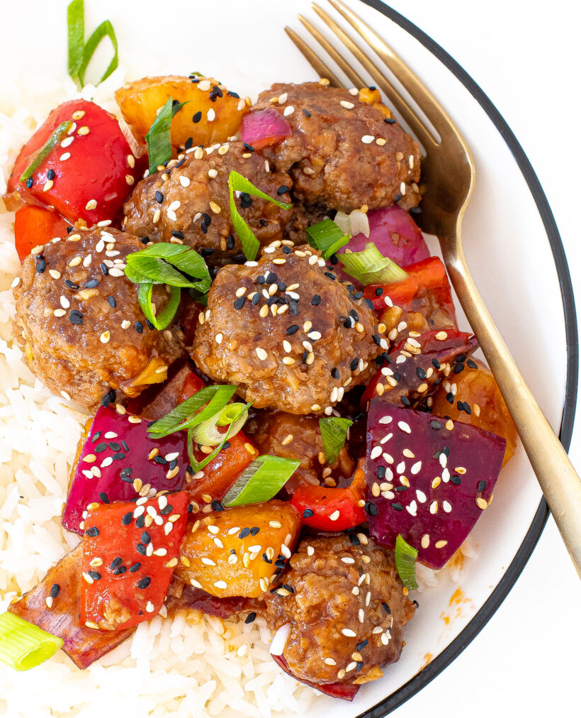 Close up view of slow cooker hawaiian meatballs on a bed of white rice on a white plate with a fork.