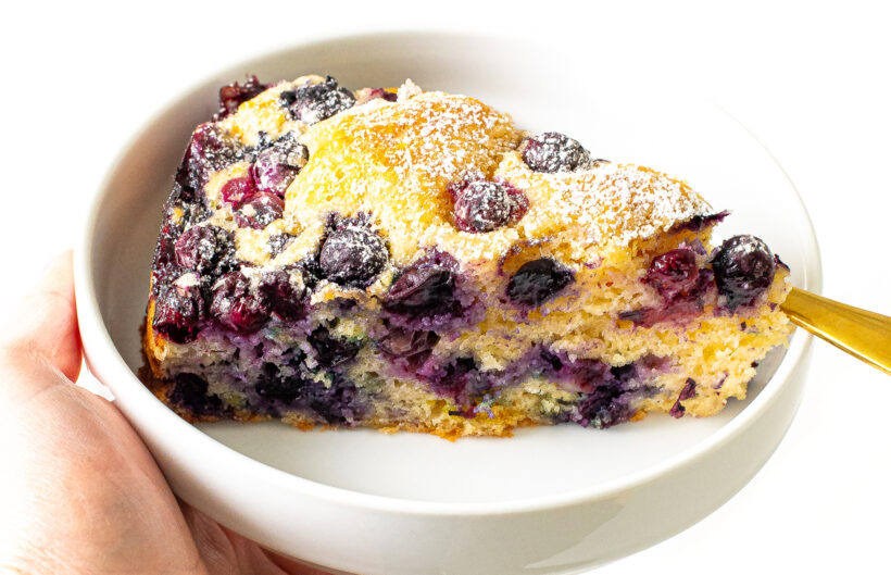 Slice of blueberry cake topped with a dusting of powdered sugar.