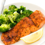 an air fryer salmon filet on a white plate with steamed broccoli and a lemon wedge | chefsavvy.com
