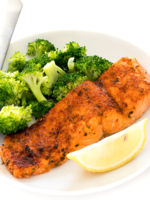 an air fryer salmon filet on a white plate with steamed broccoli and a lemon wedge | chefsavvy.com