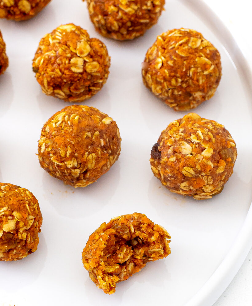 Carrot cake oat balls served on a white dish with one of them missing a bite.