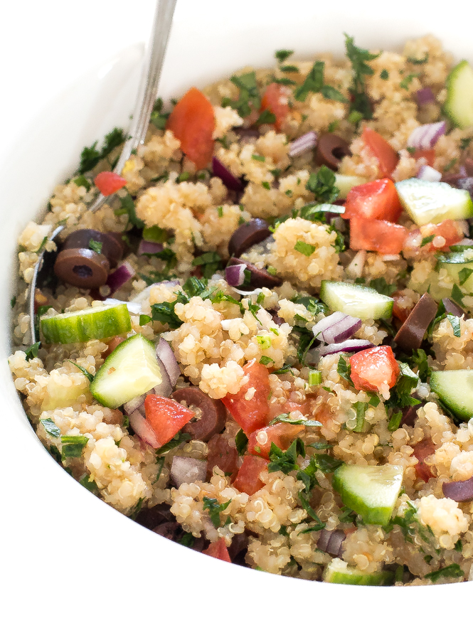 Close up of cooked grains with chopped vegetables with a spoon in a white bowl.