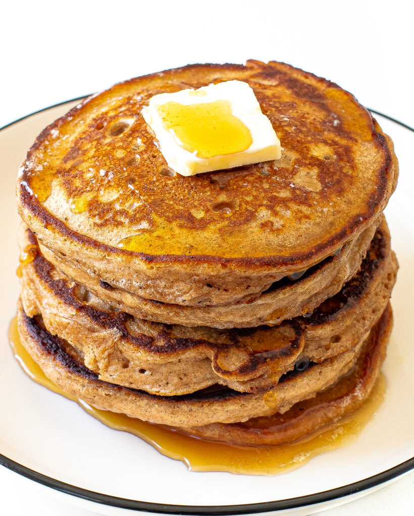 side view of a stack of healthy pancakes with maple syrup and a pat of butter on top
