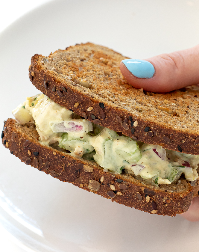 Tuna salad sandwich in a hand with a plate underneath. 