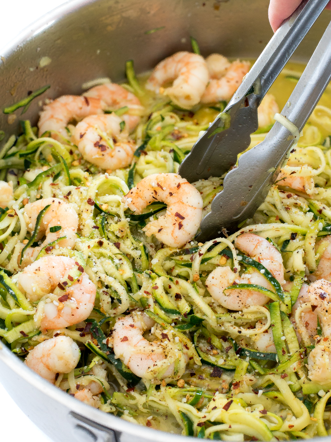 Silver tongs serving healthy shrimp scampi with zucchini noodles from a stainless steel pan.