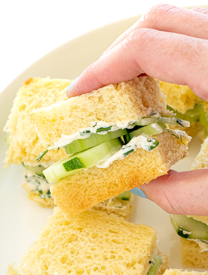 Sandwich filled with cream cheese and cucumber being held.