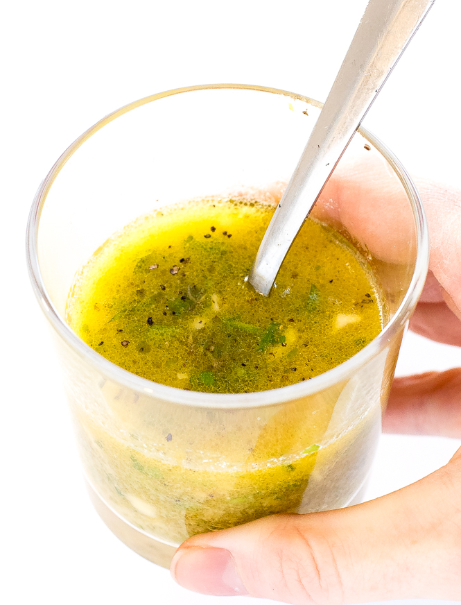 author holding a glass filled with lemon vinaigrette
