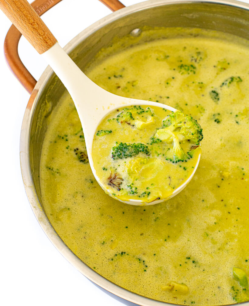 scooping high protein broccoli cheddar soup out of large pot with white ladle