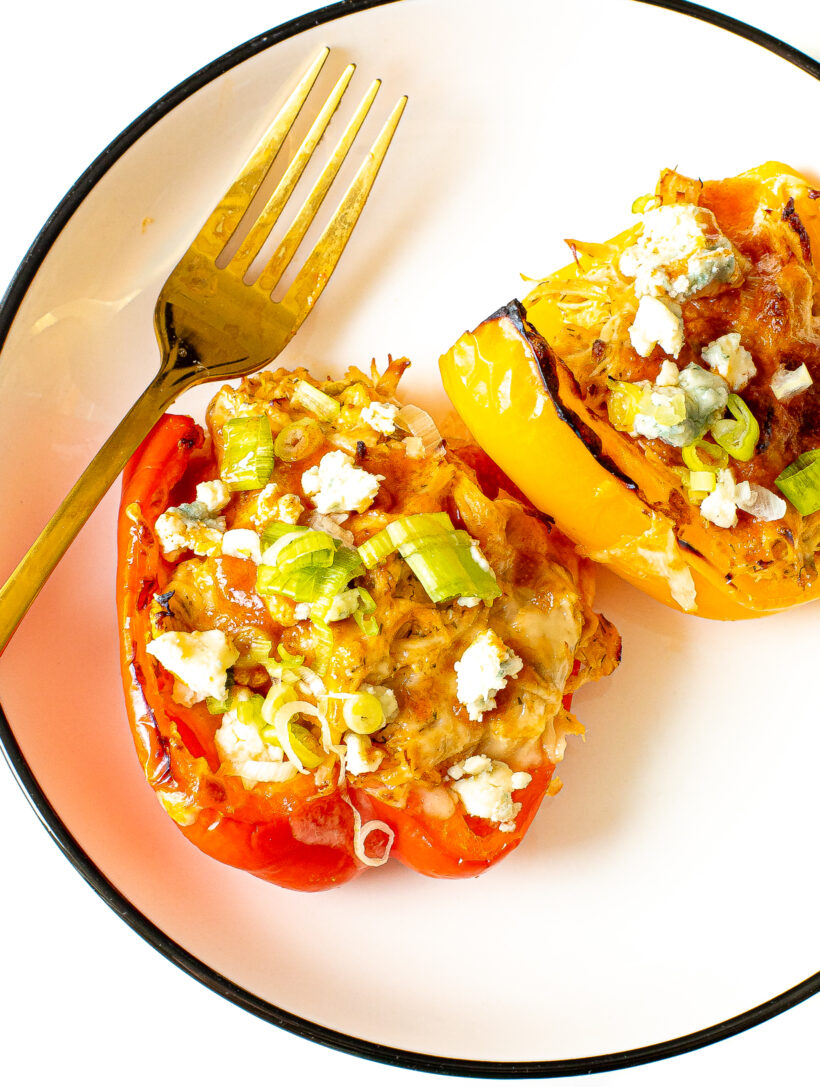Two stuffed pepper halves on a white plate with a gold fork.