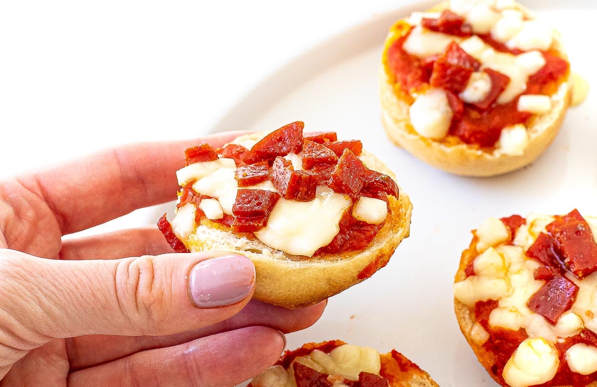 author holding mini pizza bagel with cubed pepperoni