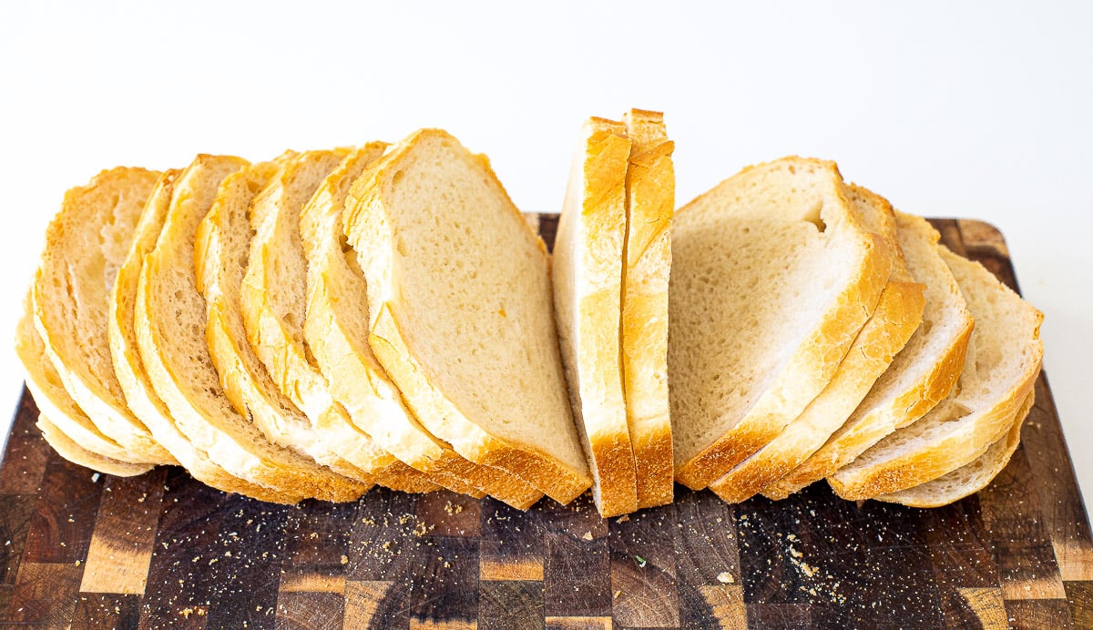 Slices of white bread arranged in a row on a wooden cutting board.