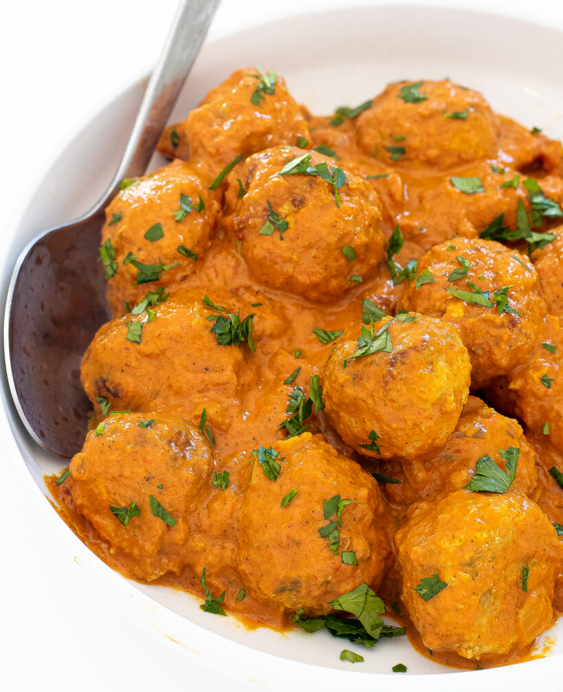 Butter chicken meatballs in a white bowl with a spoon. 