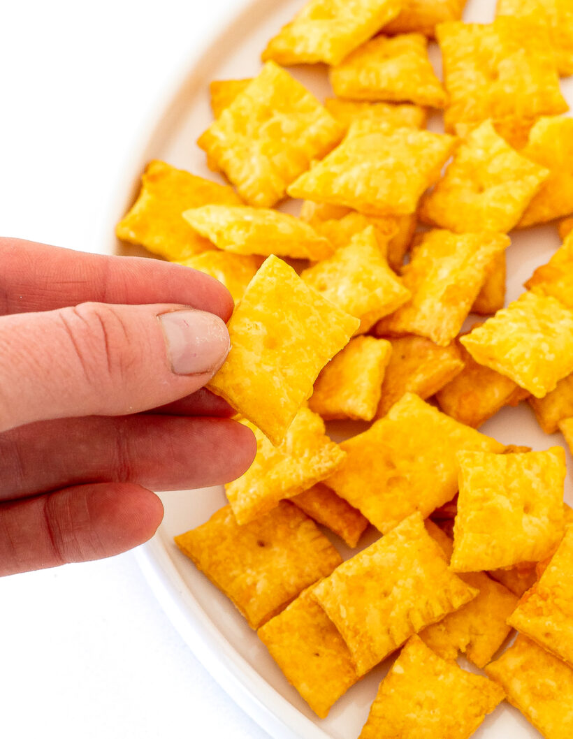 Hand holding a homemade cheez it with more in the background. 
