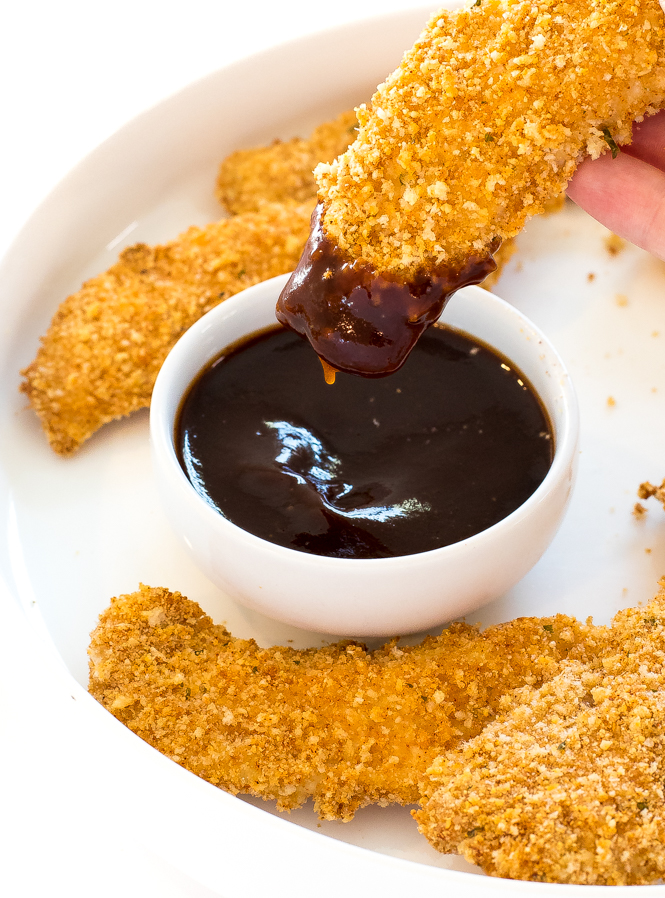 Homemade baked chicken tender being dipped in barbecue sauce