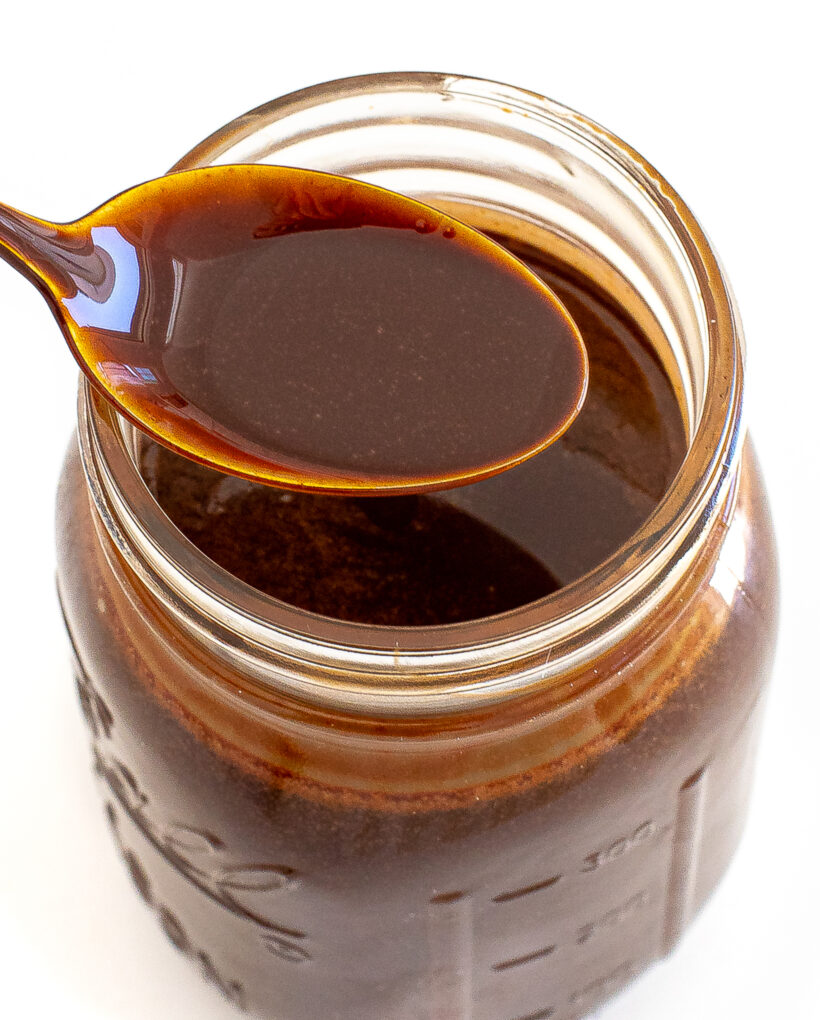 Homemade chocolate syrup in a jar with a spoon taking some from the jar. 
