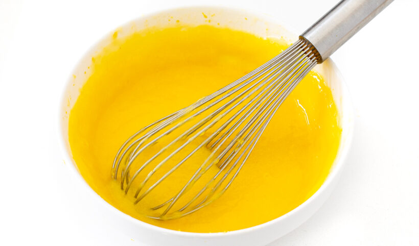 Lemon curd in a white bowl with a whisk.