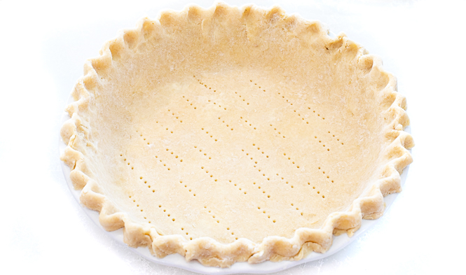 Pie dough in a pie dish with holes from a fork in the bottom. 