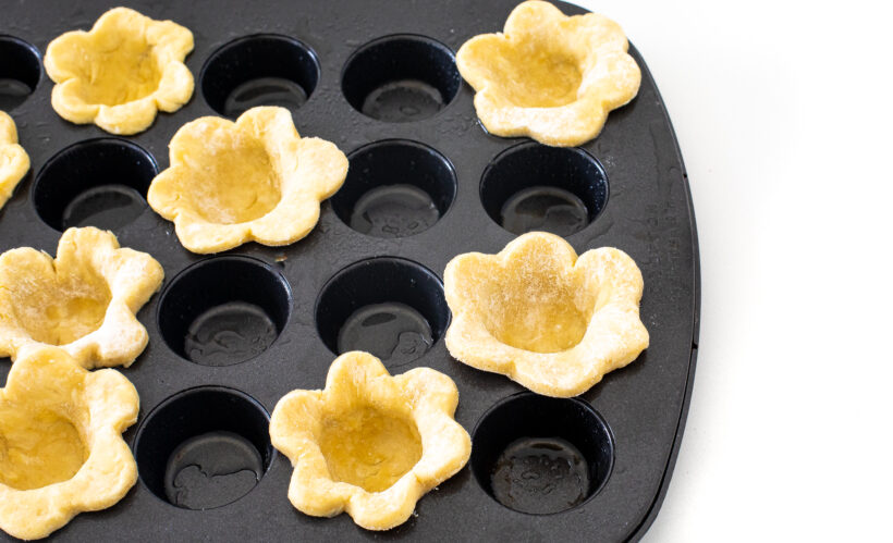 Pie dough in the shape of flowers pressed into a mini muffin tin.