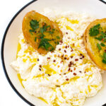 A bowl of ricotta topped with olive oil and red pepper flakes. Two pieces of crostini are in the bowl.