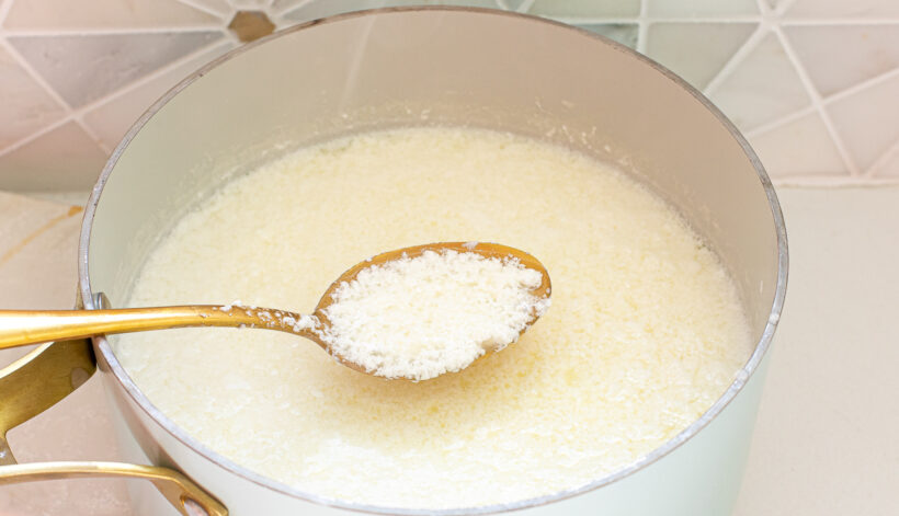 Milk that has separate into curds in a white saucepan. A gold spoon is holding up a scoop of the curds.