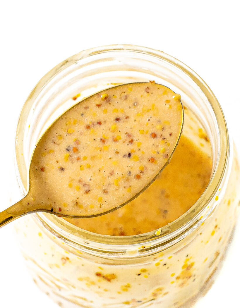 Honey mustard dressing in a glass jar with a spoon holding some of the dressing.