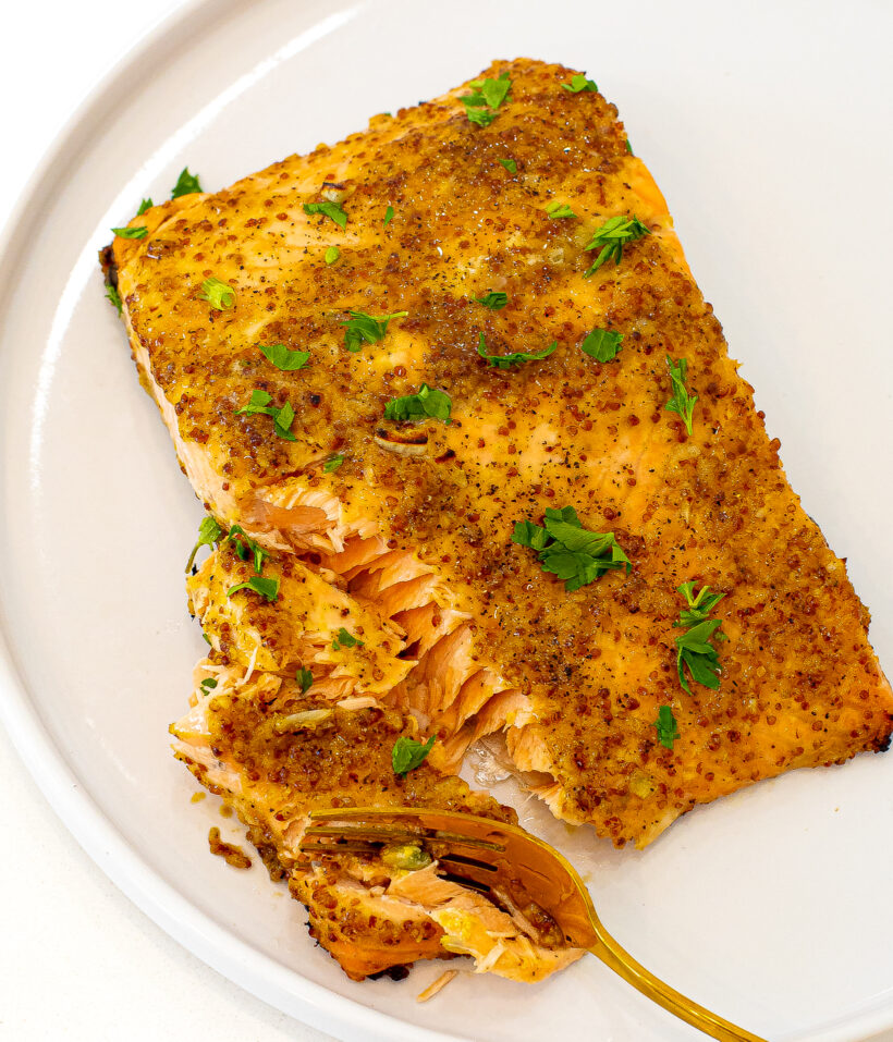 Honey mustard salmon served on a plate with a fork flaking some bites off. 