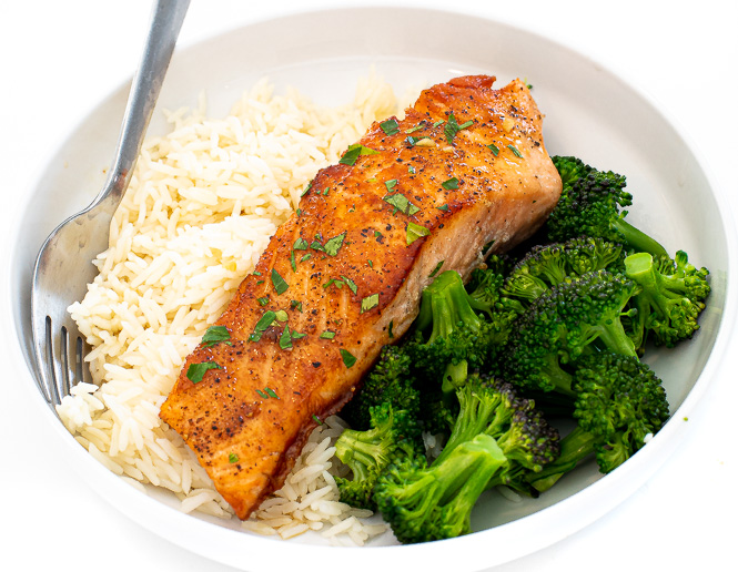 fish topped with chopped parsley in white bowl with white rice and steamed broccoli