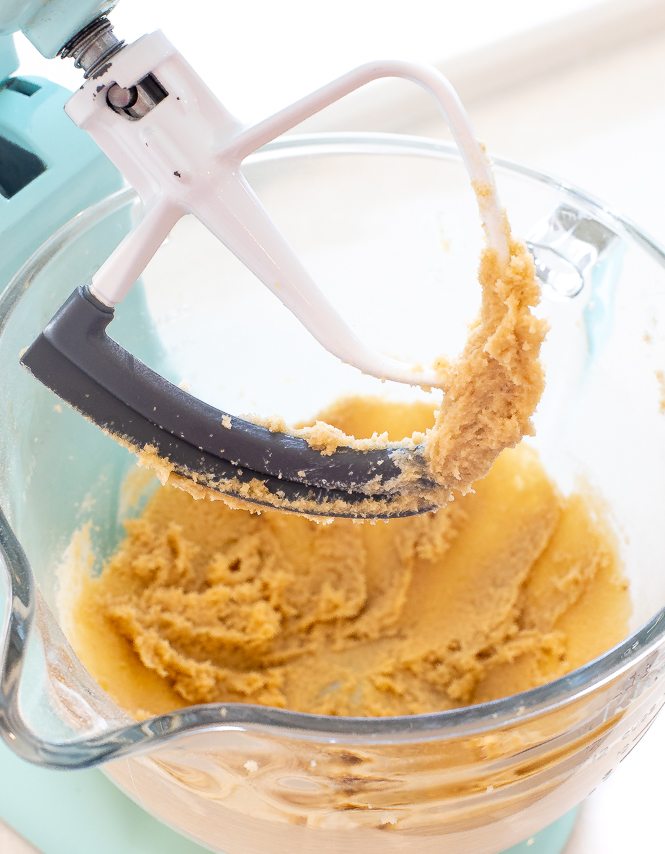 Clear mixing bowl with a paddle attachment, with creamed butter and sugar.