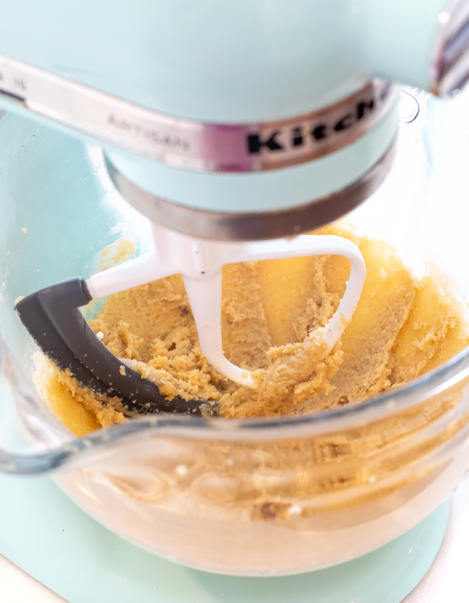 Clear mixing bowl with a paddle attachment, with creamed butter and sugar.