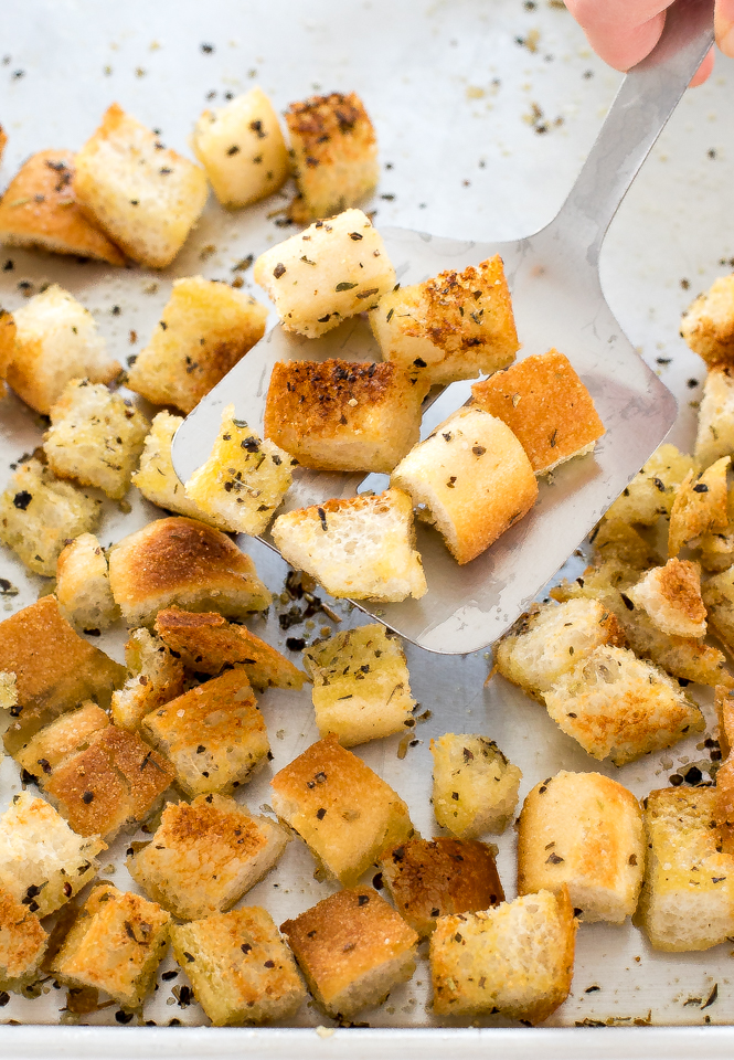 homemade croutons on a baking sheet being scooped up with a metal spatula