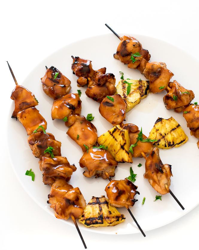 Grilled Huli Huli Chicken skewers on a white plate with pineapple.