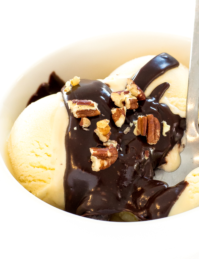 homemade chocolate sauce drizzled over a cup of ice cream with chopped walnuts on top