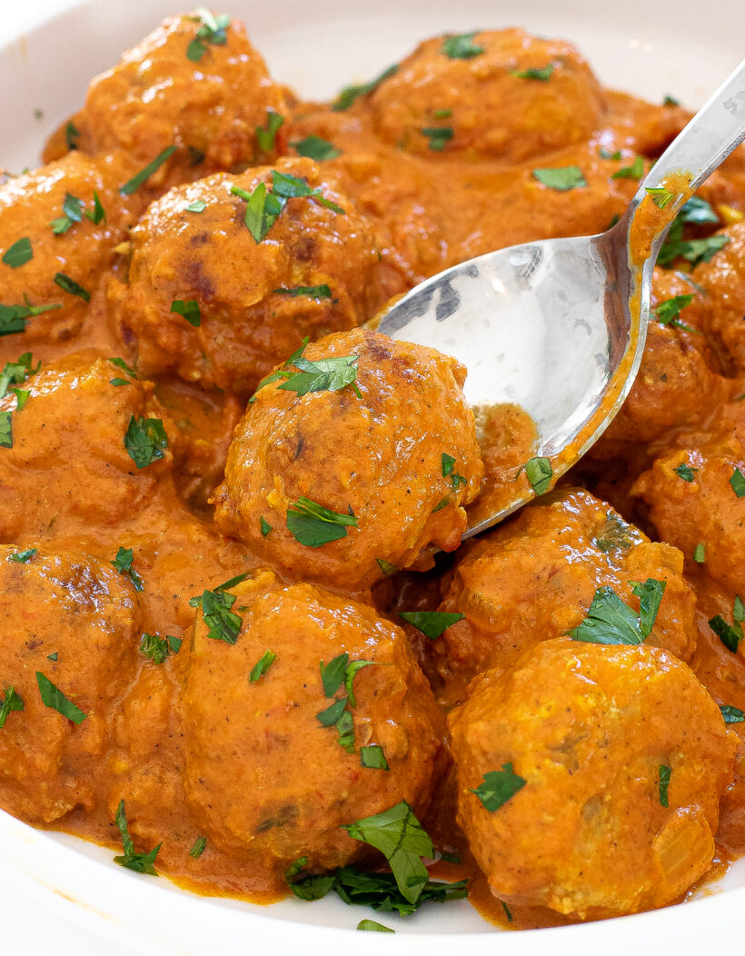 Butter chicken meatballs in a bowl with a spoon scooping one up.