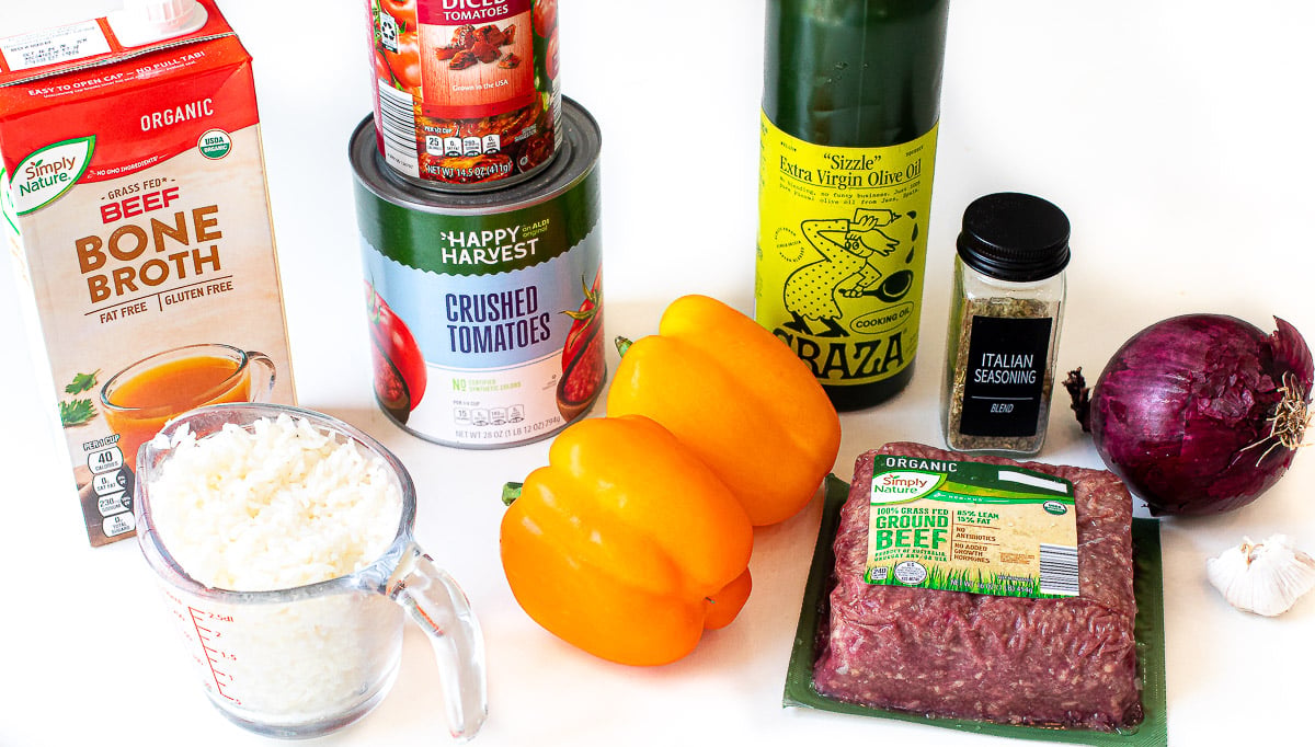 Ingredients like ground beef, bell peppers, broth, canned tomatoes, red onion and cooked rice.
