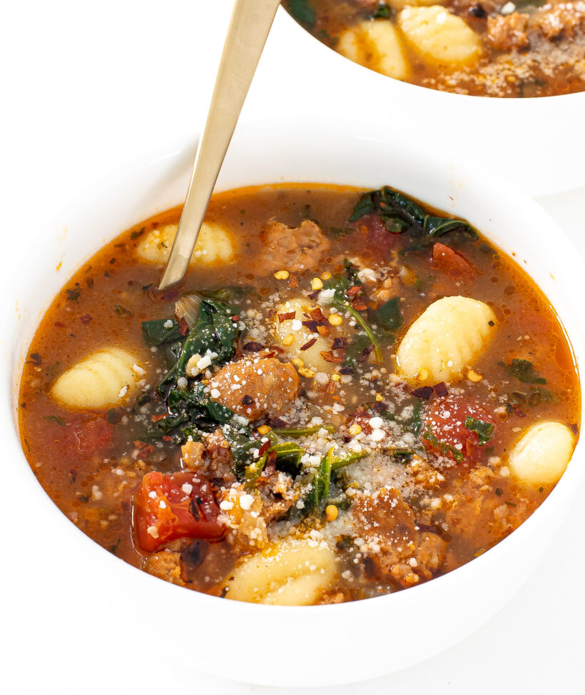 italian gnocchi soup in white bowl with crushed red pepper flakes and parmesan cheese
