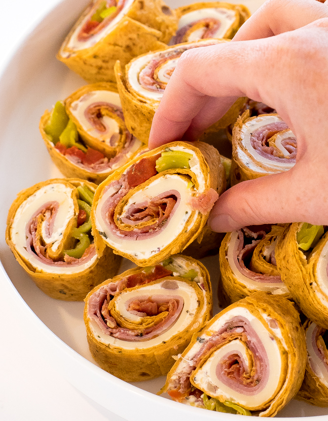 a close up of these sliced roll ups on a white platter with the author's hand selecting one to eat